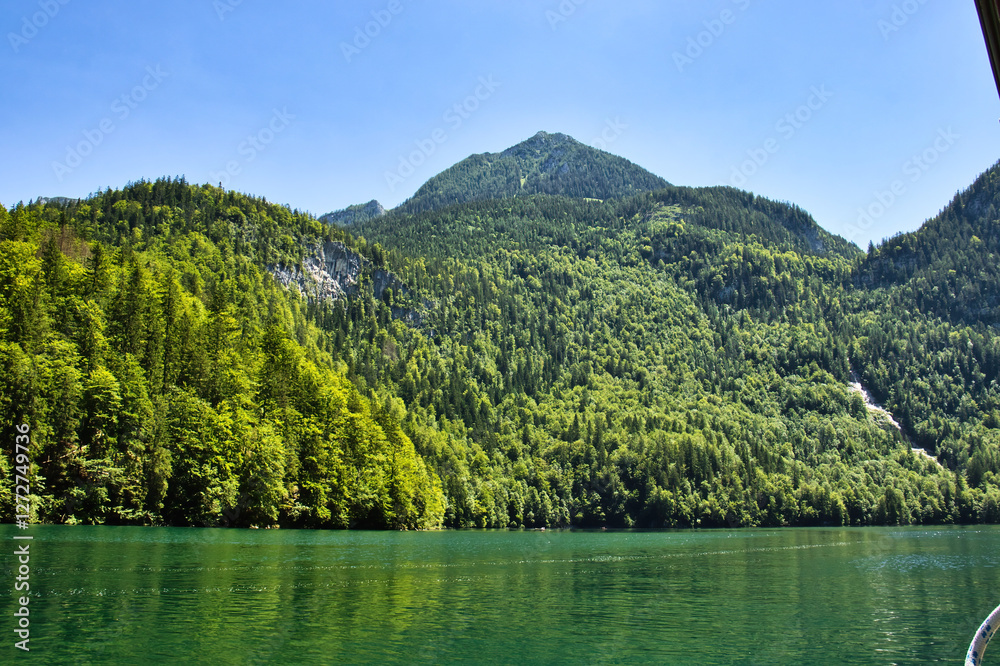 Green trees on mountainsand above green water at Konigssee in Bavaria, Germany on a sunny spring day. Green trees on mountainsand above green water at Konigssee in Bavaria, Germany on a sunny spring day.