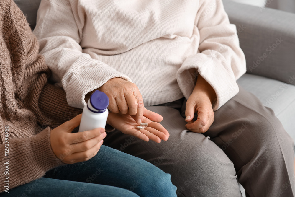 Obraz premium Young nurse giving pills to senior woman on sofa at home, closeup