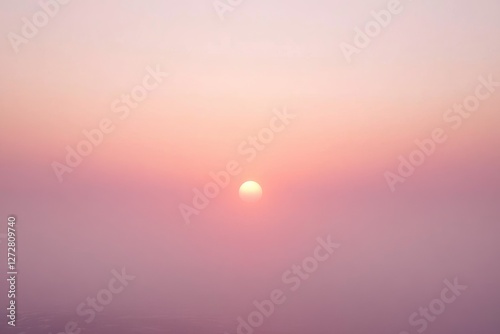 Fototapeta Naklejka Na Ścianę i Meble -  A hazy, pink sunset with a soft, muted sun centered in the frame.