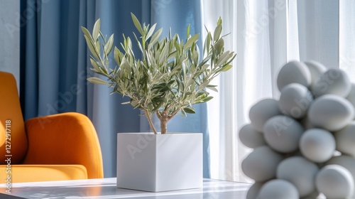 Obraz na płótnie A close-up photo of white square planters with an olive tree inside, on a table in front of blue curtains and an orange chair. w salonie
