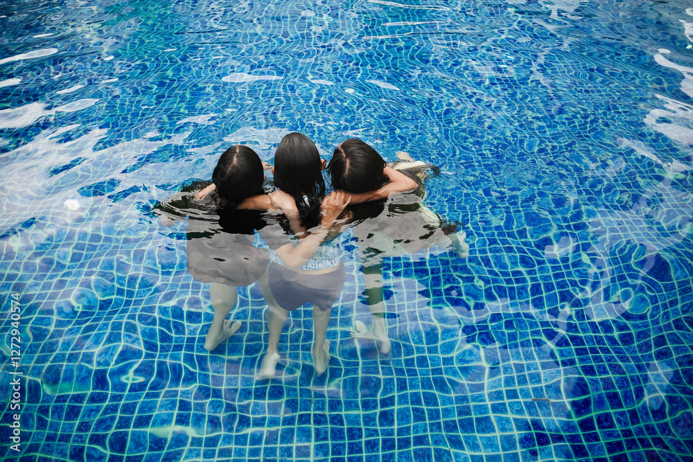 © AmpYang Images - Three Asian teenage girls playing and embracing each other inside a swimming pool
