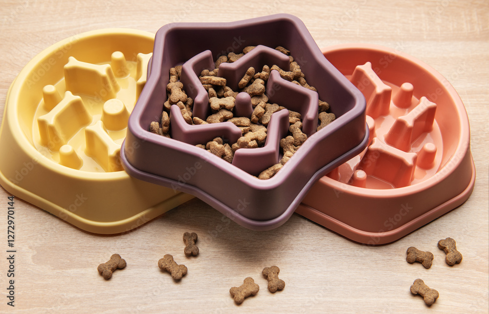 Slow feeding bowl containing dry pet food on wooden table