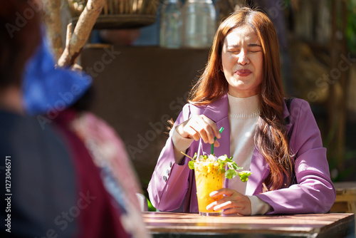 Young asian businesswoman savoring a refreshing tropical fruit juice with mint and ice at an outdoor cafe, experiencing a moment of relaxation during her workday photo