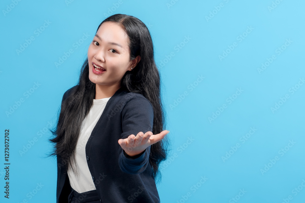 A cheerful young woman in a dark blue sweater and a white shirt gestures warmly while standing against a vivid blue background. The composition exudes a friendly and inviting atmosphere.