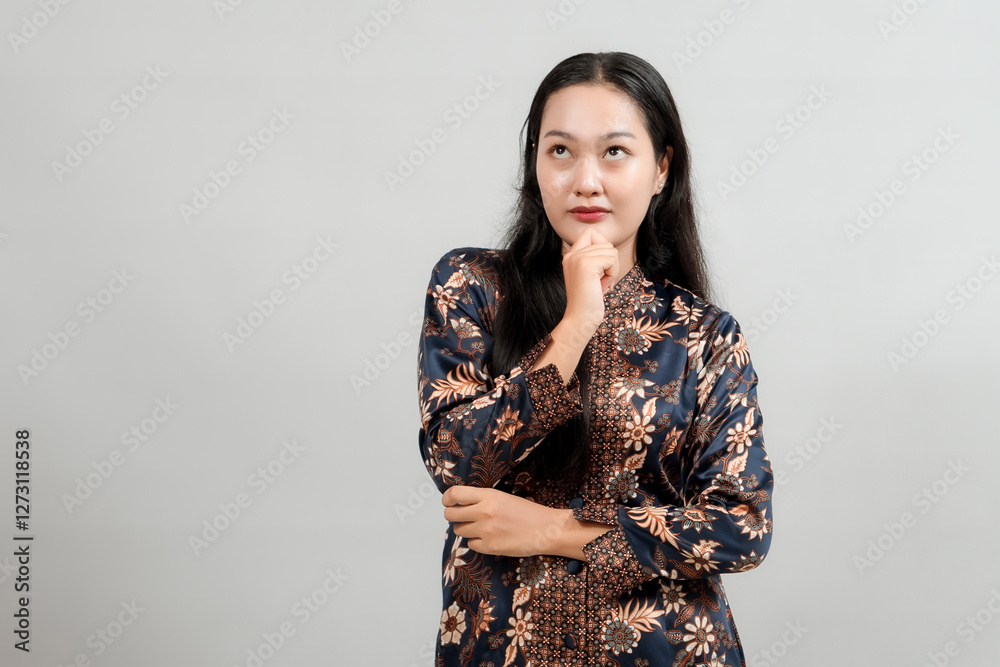 A thoughtful young woman in elegant Indonesian batik attire, touching her chin with a contemplative expression, reflecting on ideas and showcasing the beauty of traditional fashion A thoughtful young woman in elegant Indonesian batik attire, touching her chin with a contemplative expression, reflecting on ideas and showcasing the beauty of traditional fashion