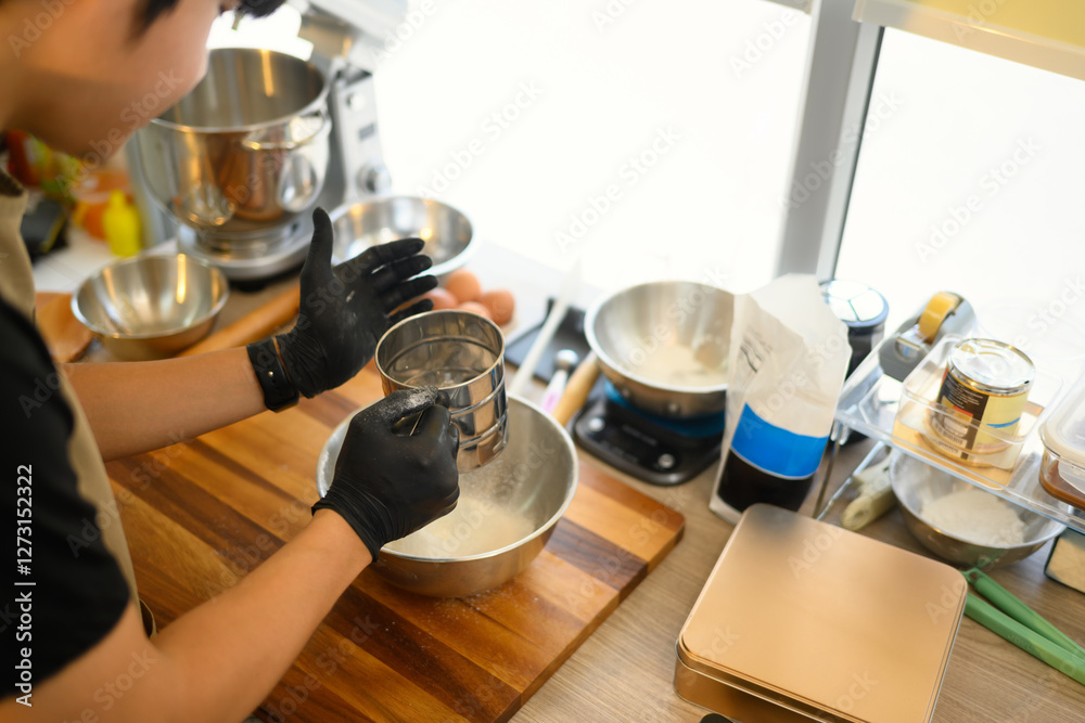 Young man sifting flour for homemade cookies in a bright kitchen Young man sifting flour for homemade cookies in a bright kitchen