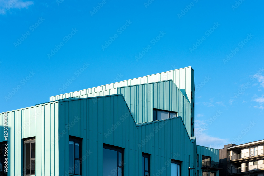Modern turquoise metal-clad buildings with angular rooflines under a deep blue sky, highlighting contemporary architecture. Modern turquoise metal-clad buildings with angular rooflines under a deep blue sky, highlighting contemporary architecture.