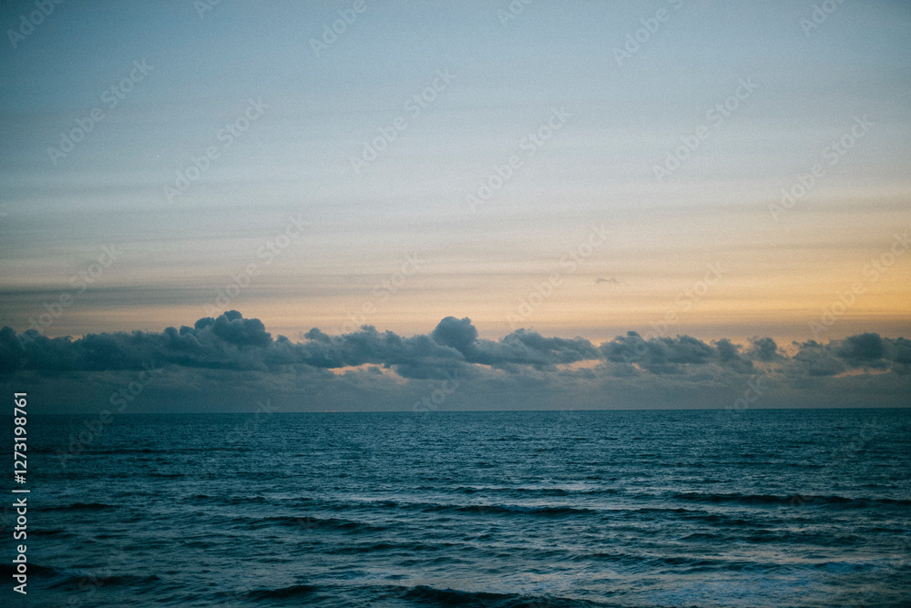 The sky is blue and the ocean is calm. The clouds are white and scattered across the sky The sky is blue and the ocean is calm. The clouds are white and scattered across the sky