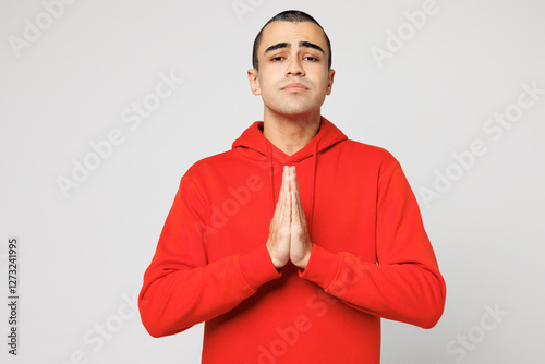 Young sad middle eastern man he wear red hoody casual clothes hold hands folded in prayer gesture, begging about something isolated on plain solid white background studio portrait. Lifestyle concept. photo