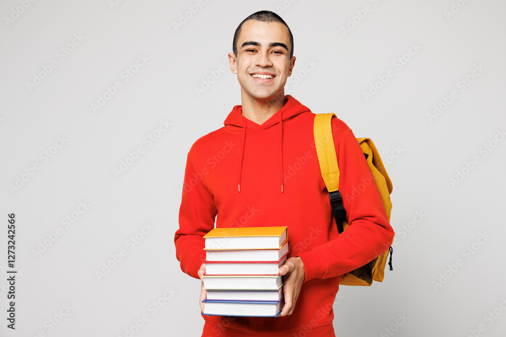 Young smart smiling middle eastern man boy student he wear red casual clothes backpack bag hold in and stack of books isolated on plain solid white background. High school university college concept. Young smart smiling middle eastern man boy student he wear red casual clothes backpack bag hold in and stack of books isolated on plain solid white background. High school university college concept.