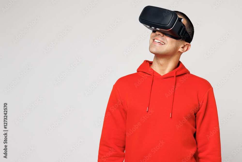 Young smiling happy middle eastern man he wears red hoody casual clothes watching in vr headset pc gadget play video game isolated on plain solid white background studio portrait. Lifestyle concept. Young smiling happy middle eastern man he wears red hoody casual clothes watching in vr headset pc gadget play video game isolated on plain solid white background studio portrait. Lifestyle concept.