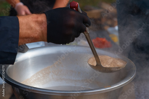 A cook's assistant collects foam from a cauldron on the surface of meat soup with a slotted spoon. Technology of food preparation. The concept of public catering.