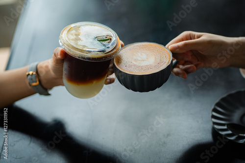 Fotografie Hands of teenage girls holding glass of ice coffee and cup of hot coffee together at cafe
