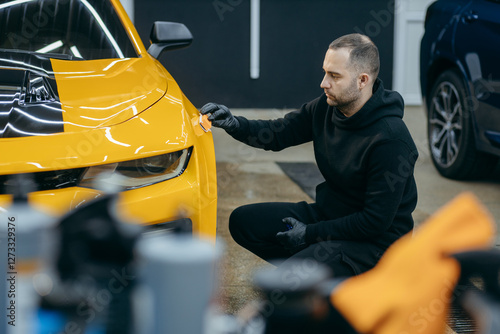 Car detailing worker applying ceramic car coating on yellow car at workshop
