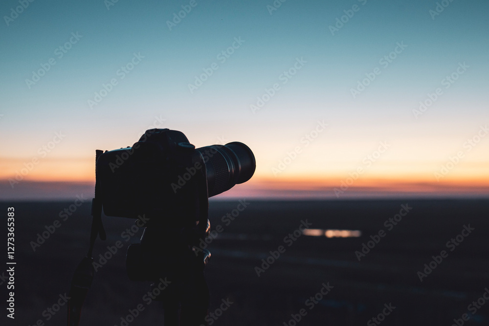 Obraz premium camera at sunset on tripod shooting beautiful sunny horizon with long exposure, background blurred with bokeh effect