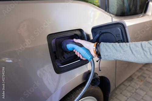 Charging electric car, female hand holding plug and connecting it to the vehicle photo