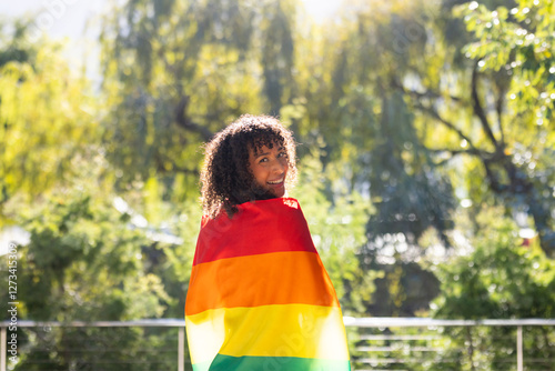 Smiling woman wrapped in rainbow flag standing outdoors, enjoying sunny day photo