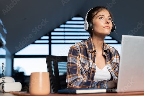 Young woman wearing headphones using laptop, sitting at home desk