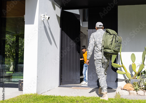 Returning home, soldier in uniform with backpack greeted by young son at door, copy space photo