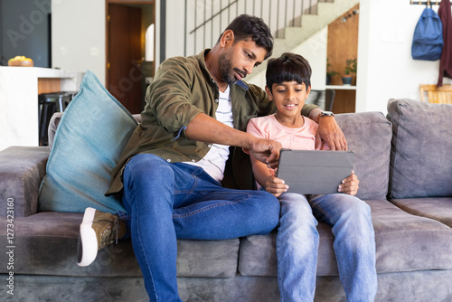 indian father and son sitting on couch using tablet, bonding and learning together