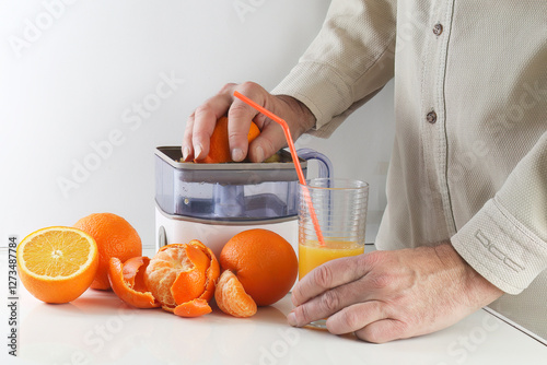 Man squeezing an orange in a juicer with some ripe oranges  and glass of feesh juice with a straw on white kitchen photo