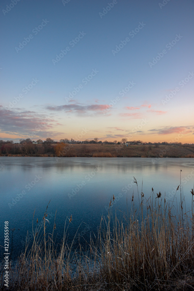 Obraz premium Beautiful blue hour on the lake, trees on the beach , sunrise over the lake with blue sky without clouds.Landscape photography on the pond , purple colors on the sky , trees and water , reflections 