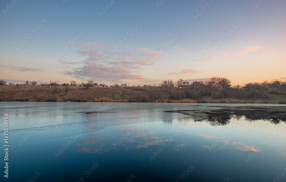 Fototapeta premium Blue hour on the lake , beautiful landscape photography on the lake with sunrise and reflactions on water , trees on the beach of the lake ,blue and orange colors.Blue sky . Water reflections 