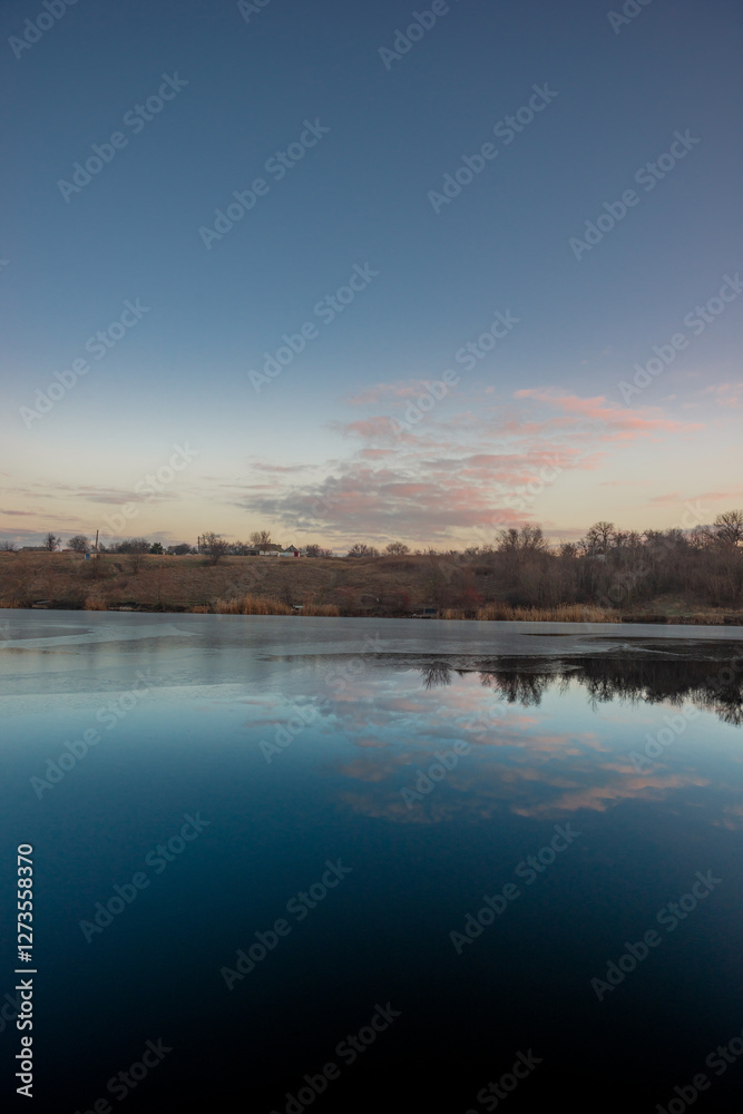 Fototapeta premium Blue hour on the lake , beautiful landscape photography on the lake with sunrise and reflactions on water , trees on the beach of the lake ,blue and orange colors.Blue sky . Water reflections 