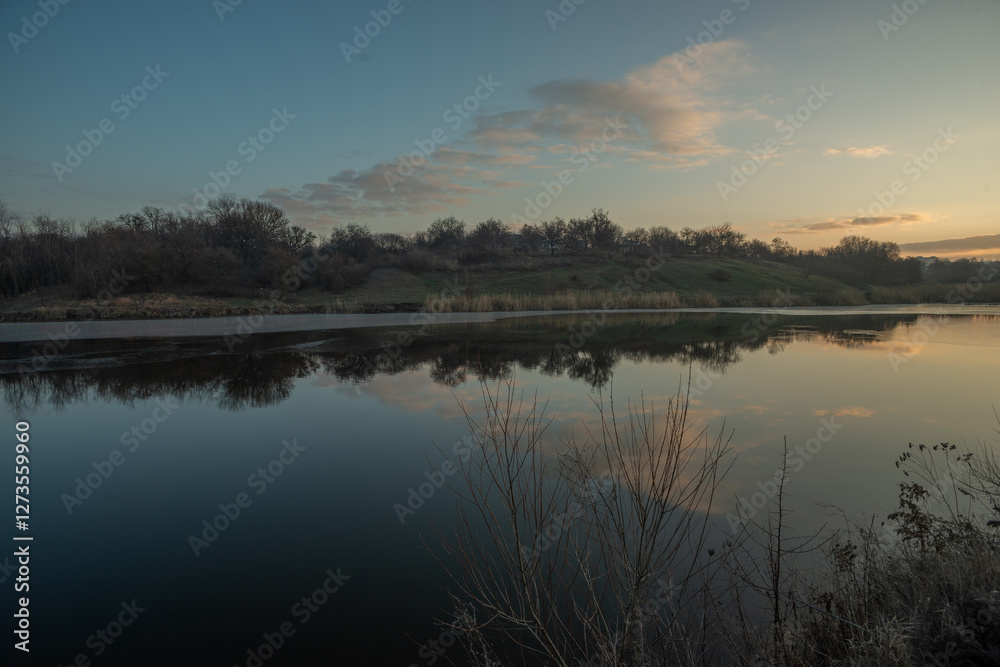 Obraz premium Beautiful sunrise on the pond , pond near the village .Red and orange sunrise in the sky , trees and houses , landscape on the lake with sunrise , reflactions on water 