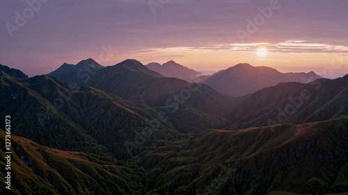 A colorful sunrise over a mountain range, casting golden light on the panoramic landscape filled with lush nature.
