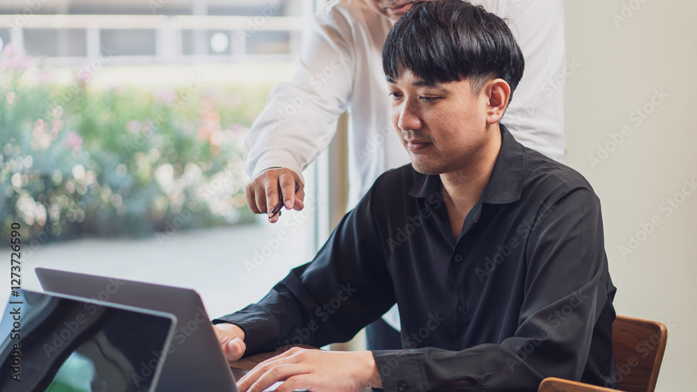 workplace collaboration, guidance, featuring a man working on a laptop while another person points at the screen, providing instruction or feedback. coaching, leadership, and business communication.