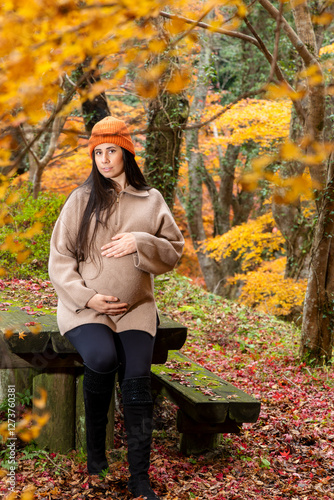 A beautiful 8-month pregnant woman taking pictures in a beautiful park in the middle of autumn photo