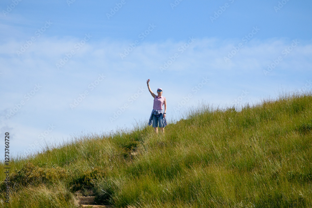 Woman in sunglasses standing on grassy field and waving Woman in sunglasses standing on grassy field and waving