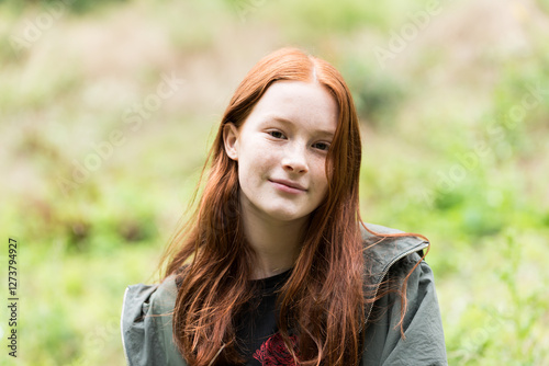Red haired twelve year old girl with freckles posing with a nature bokeh background