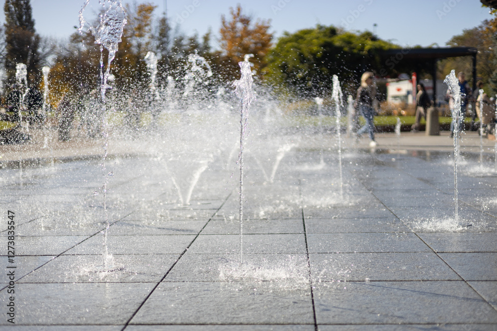 Water droplets spread from the fountain in the air. Splashing water from a fountain in the park. Vertical fountain jets in the sidewalk on the square in the city park.