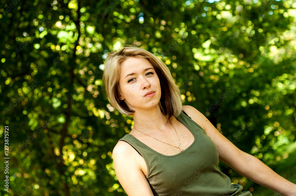 Blonde girl in a green T-shirt and jeans sits on a log in the park Blonde girl in a green T-shirt and jeans sits on a log in the park