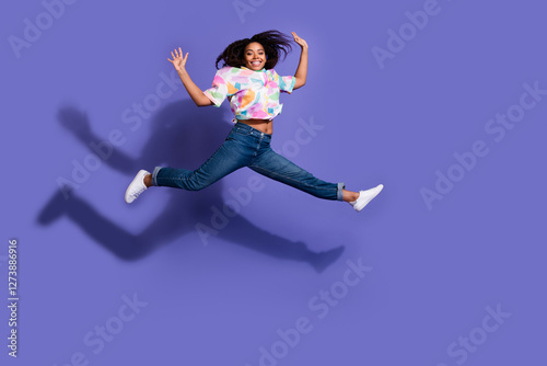 Young woman leaping joyfully against a vibrant purple backdrop, showcasing a colorful casual style