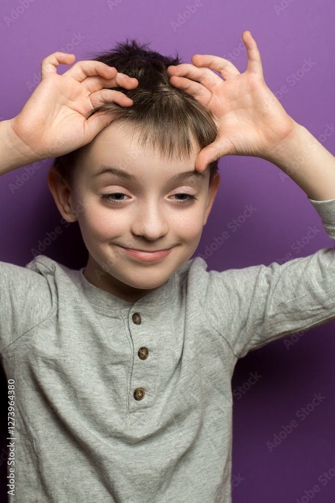 Child making bunny ears with hands, playful gesture against purple background. Great for themes of childhood fun, imagination, playful moments, and innocence.