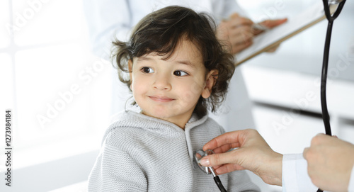 Woman-doctor examining a child patient by stethoscope. Cute arab toddler at physician appointment. Medicine concept