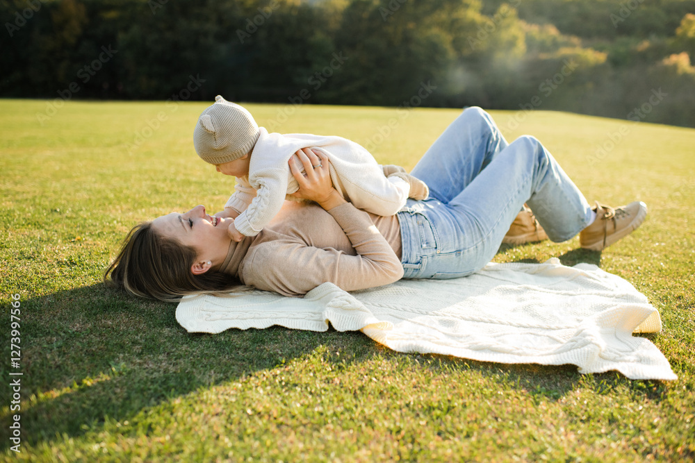Mother holding cute baby boy lying on green grass lawn and playing together outdoor. Summer season. Motherhood. Mother holding cute baby boy lying on green grass lawn and playing together outdoor. Summer season. Motherhood.
