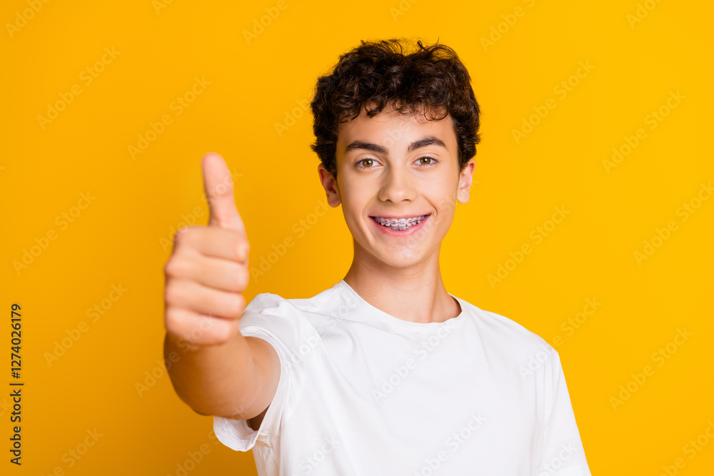 Smiling Teen Boy Showing Thumb Up Gesture in Casual White Shirt on Vibrant Yellow Background Smiling Teen Boy Showing Thumb Up Gesture in Casual White Shirt on Vibrant Yellow Background