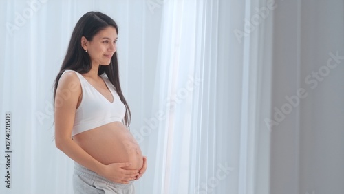 Young happy Asian pregnant woman posing in studio with white curtains in background Free Download Young happy Asian pregnant woman posing in studio with white curtains in background - GFXLoad