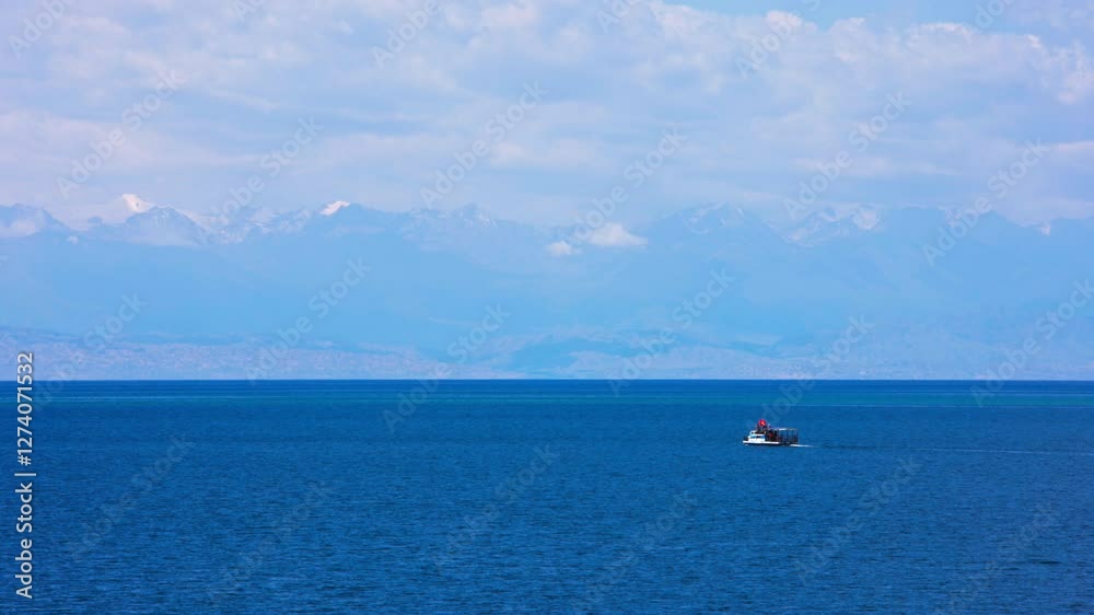 Small white passenger cruise boat on Lake Issyk-Kul, Kyrgyzstan, with stunning snow-capped mountains in the background. The calm blue water and clear sky create a peaceful and scenic landscape. Small white passenger cruise boat on Lake Issyk-Kul, Kyrgyzstan, with stunning snow-capped mountains in the background. The calm blue water and clear sky create a peaceful and scenic landscape.