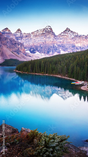 Moraine Lake at dawn, reflecting majestic mountains and pine forests in its crystal-clear blue waters. A peaceful and breathtaking Canadian Rockies landscape.