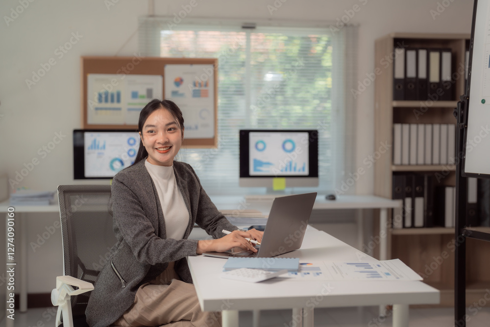 Businesswoman sitting at a desk in a modern office, using a laptop. Charts and graphs displayed on screens in the background, indicating a focus on data analysis and productivity Businesswoman sitting at a desk in a modern office, using a laptop. Charts and graphs displayed on screens in the background, indicating a focus on data analysis and productivity