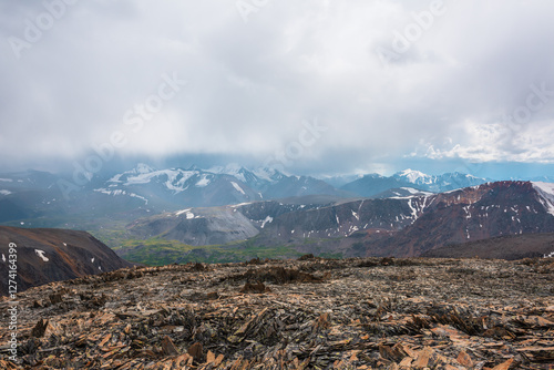 Dramatic top view from sunlit stony pass to vivid green alpine valley in sunl...