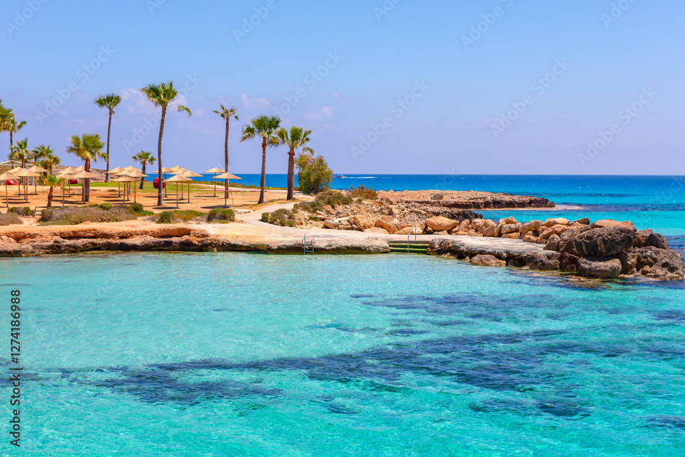 Tropical beach scene with turquoise water, rocky outcrops, and sandy shore lined with palm trees and sun umbrellas. Coastal inviting and idyllic location, good for relaxation and leisure activities