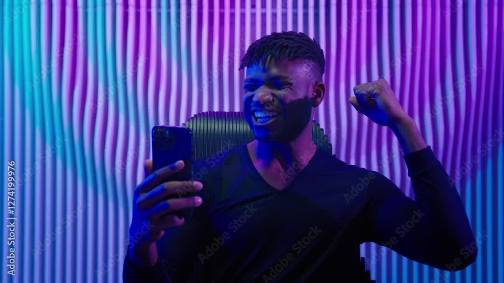 African American man guy male indoors futuristic innovation cyberspace neon lights winning with mobile phone bet casino online crypto win victory champion celebrate yelling happy video game addict