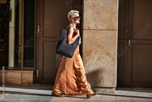 Tableau sur toile Stylish Mature Woman with Short Hairstyle Walks, Wearing Summer Beige maxi Dress and Large black Handbag