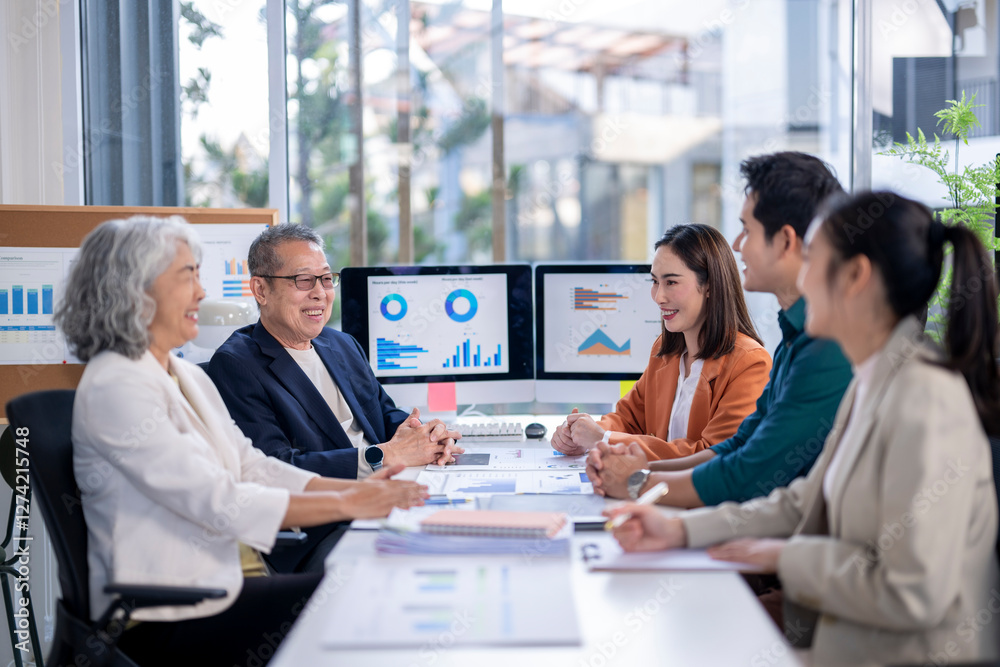 A group of people are sitting around a table with monitors and papers A group of people are sitting around a table with monitors and papers